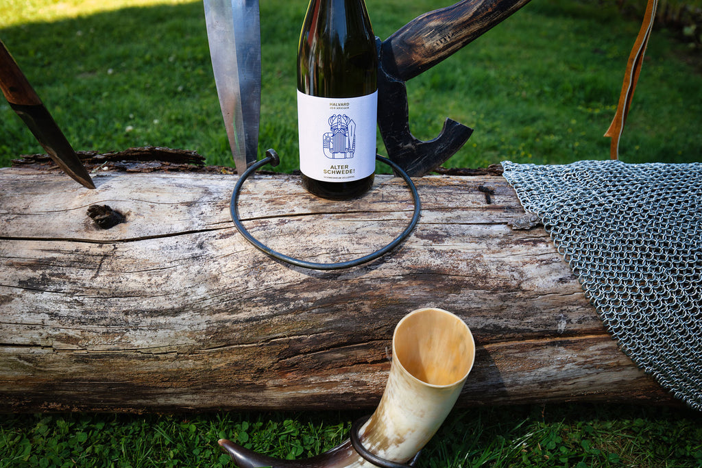 Weißwein Halvard - Alter Schwede von Weingut Schwedhelm - Zellertal - Flasche auf Baumstamm mit Axt, Kettenhemd und Wikinger Horn