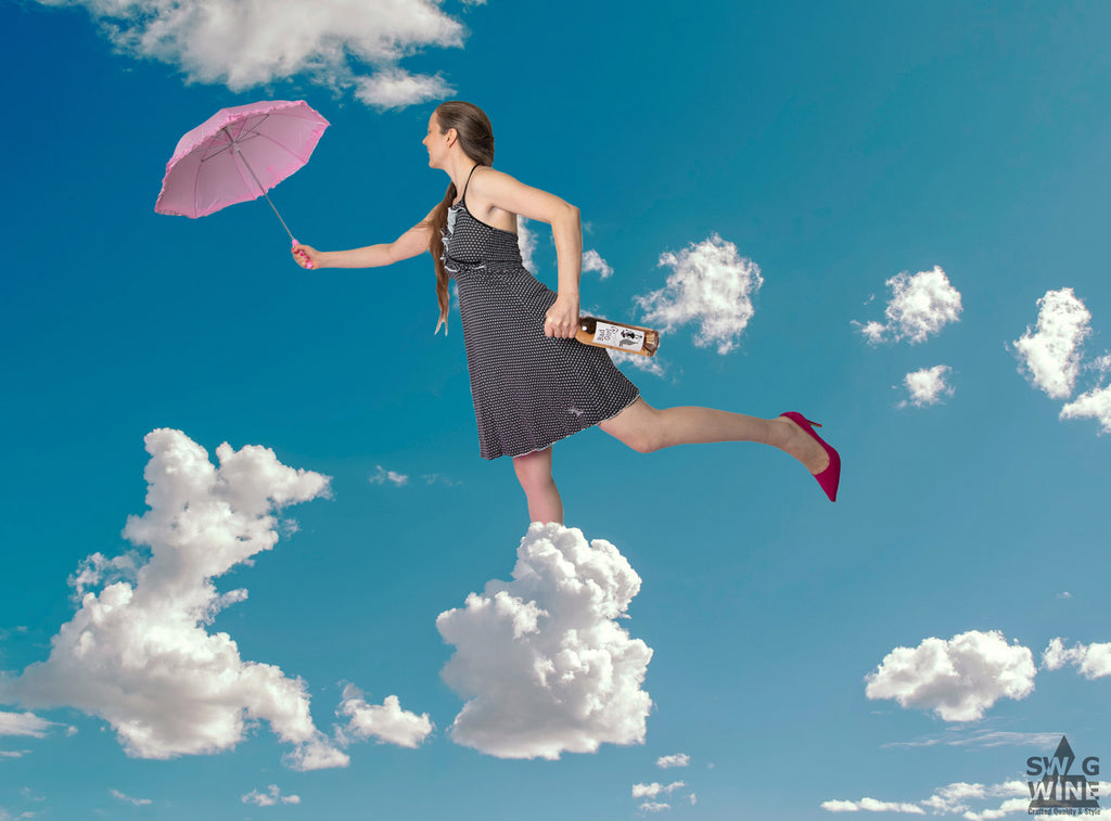 Bad Girl Rosé Bordeaux von Thunevin Frau mit Flasche in Hand und rosa Schirm läuft auf Wolken im Himmel