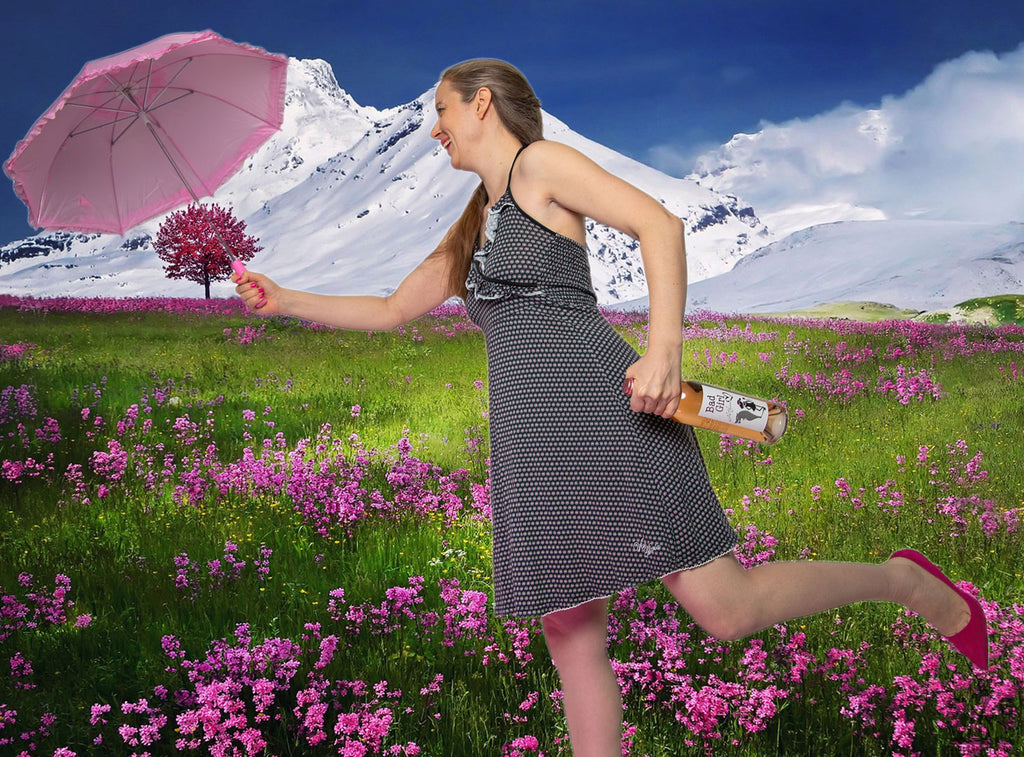 Bad Girl Rosé Bordeaux von Thunevin - Heidi mit Flasche in der Hand und rosa Schirm in einer Alpenlandschaft auf Wiese
