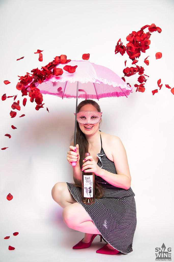 Bad Girl Rosé Bordeaux Frau mit MAske und Schirm im Regen aus Rosenblättern mit Weinflasche in der Hand