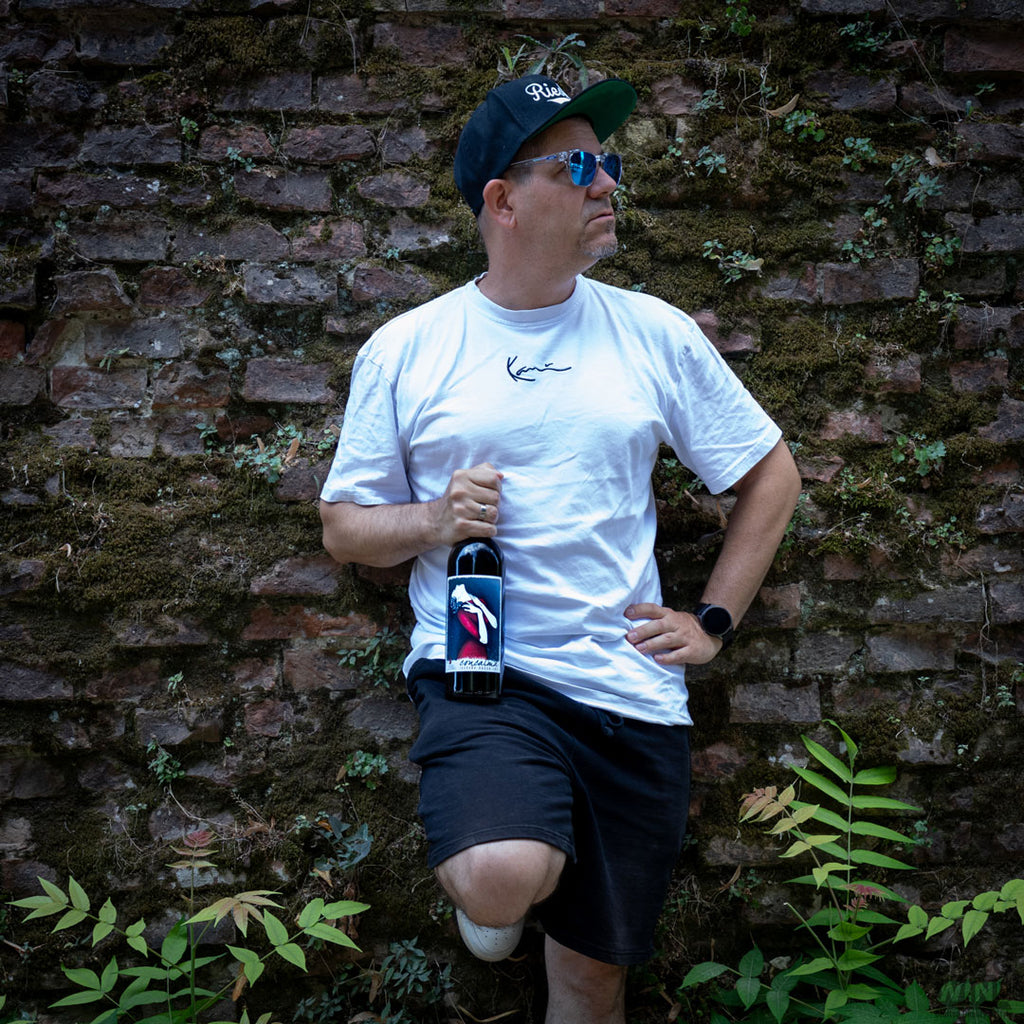 Concalma Rotwein aus der Toskana von Il Drago e la Fornace - Lifestyle Flasche in Hand eines Mannes cool an eine Mauer gelehnt