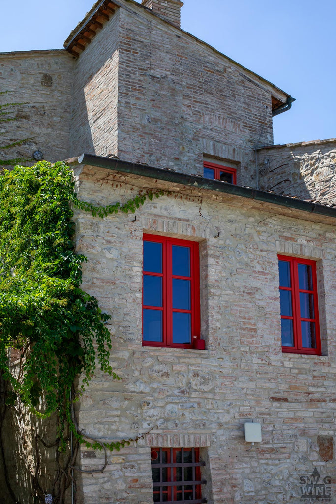 Weingut Il Drago e la Fornace Gebäude in der Toskana mit Steinen und roten Fenstern und Weinreben bewachsen
