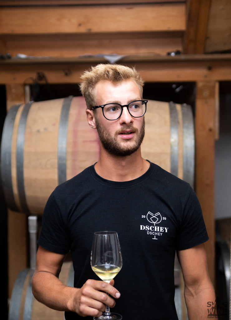 Winzer Jakob Julier von Dschey-Dschey Wines im Weinkeller mit einem Glas Weißwein vor Weinfässern