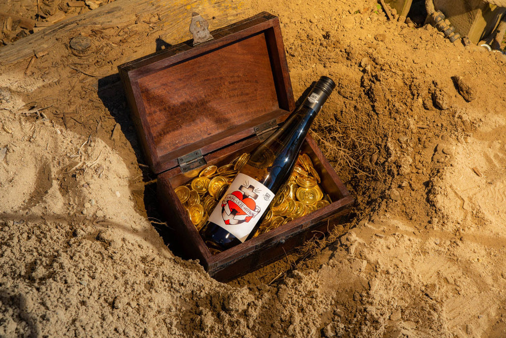 Riesling Glaube Liebe Hoffnung von Bergdolt-Reif und Nett aus der Pfalz - Flasche in vergrabener Schatztruhe mit Goldmünzen