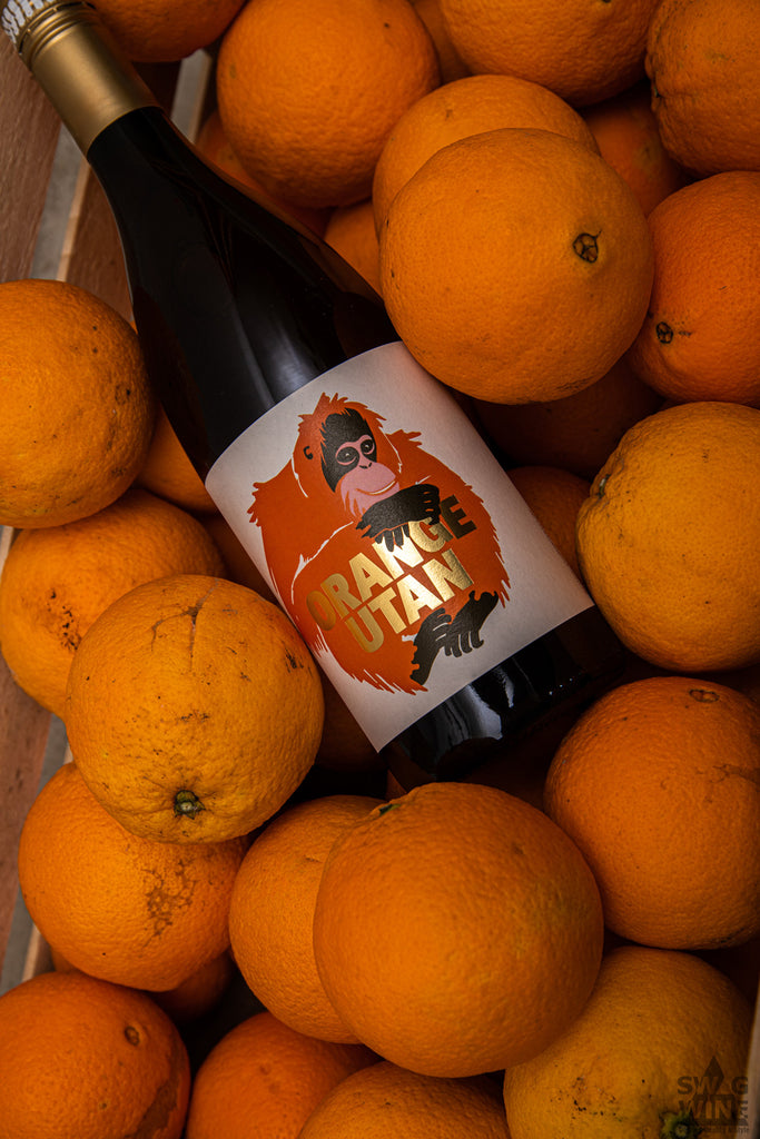 Orange Utan Wein von Swagwine - Flasche mit orangenem Orang-Utan und goldener Schrift in einer Kiste mit Orangen
