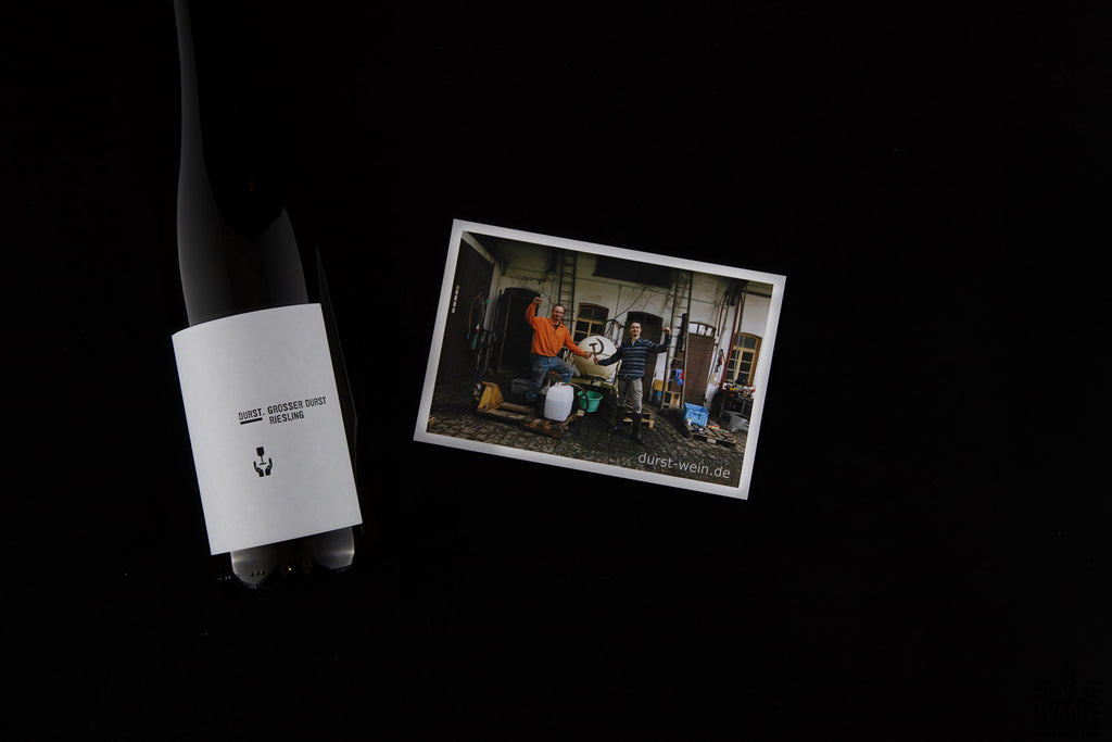Riesling Großer Durst von Andreas Durst - Weinflasche mit minimalistischem Etikett neben einer Postkarte von Durst-Wein