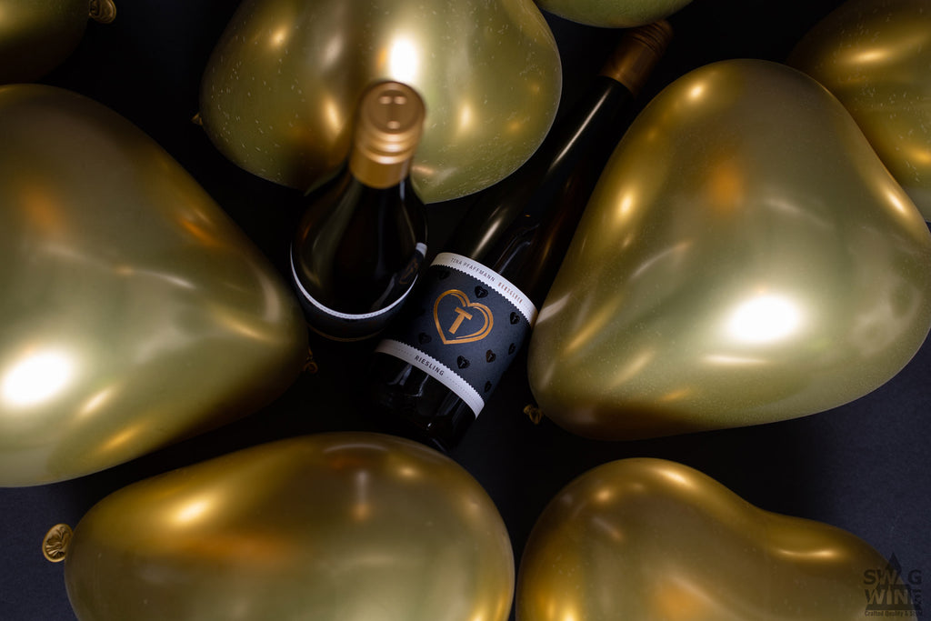 Riesling Herzglück von Tina Pfaffmann -Pfalz - Weinflaschen liegen zwischen goldenen Herz Luftballons