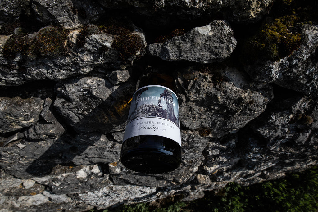 Riesling Schwarzer Herrgott von Weingut Schwedhelm im Zellertal - Flasche hängt in Felswand aus Kalk