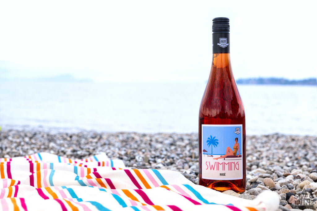 Swimming Rosé Wein von Bergdolt-Reif & Nett aus der Pfalz - Weinflasche am Strand neben Handtuch