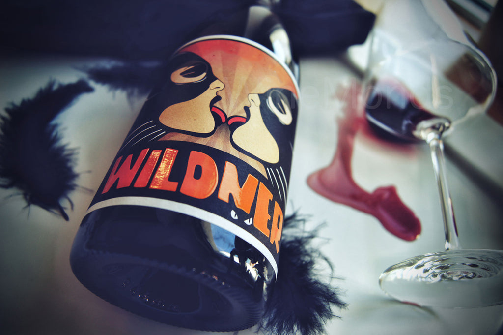 Rotwein Red Cat von Weingut Wildner aus Rheinhessen - umgekipptes Glas mit Rotweinfleck neben Federn Flasche mit maskierten Frauen