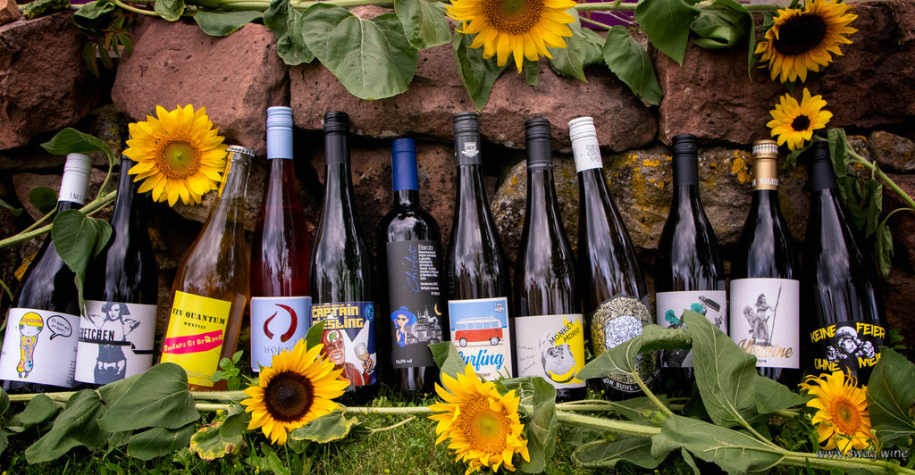 Weine von Swagwine mit ausgefallenen Etiketten an einer Sandsteinmauer mit Sonnenblumen