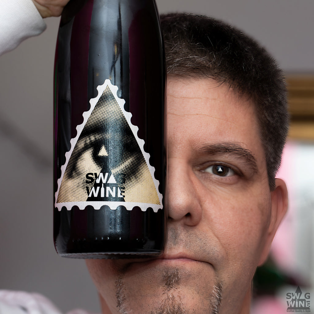 SWAGWINE Selection Weiss Riesling Rheingau Berg Schlossberg Flasche mit Auge auf dreieckigem Etikett vor Gesicht gehalten