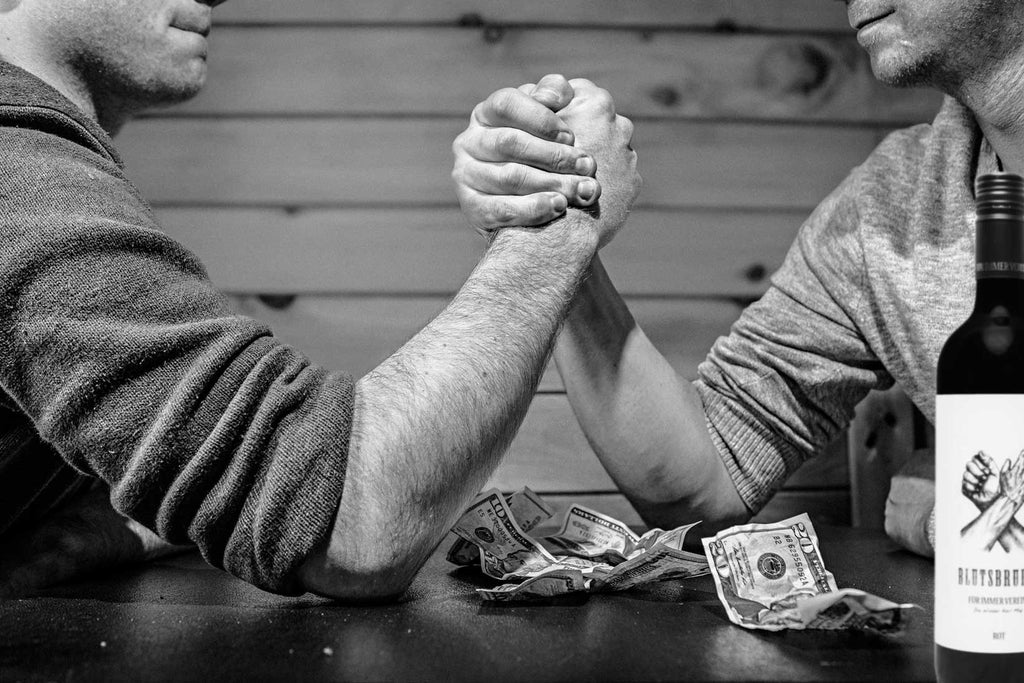 Blutsbruder rot Rotwein von Karl May - zwei Männer beim Armdrücken mit Weinflasche im Vordergrund 
