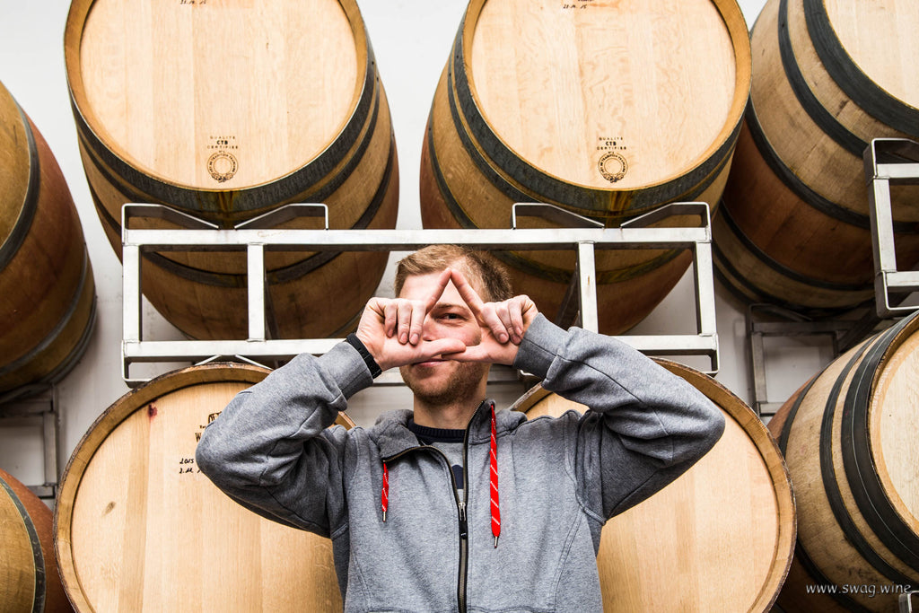 Winzer Georg Meier aus Weyher in der Pfalz zeigt das Swagwine Zeichen vor Weinfässern - Das Auge trinkt mit