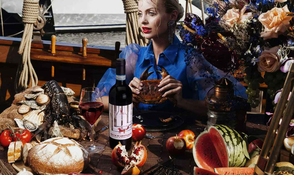 Rosso di Montalcino Sangiovese aus der Toskana von Il Drago e la Fornace Weinflasche auf einem gedeckten Tisch mit bst und Meeresfrüchten und einer eleganten Frau