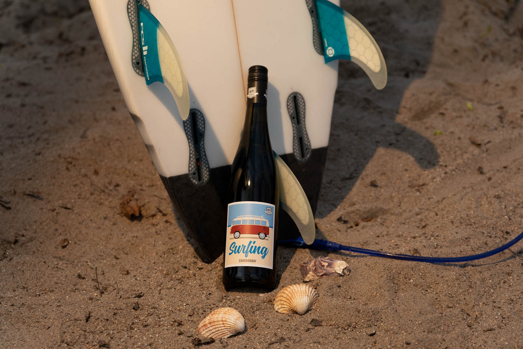 Surfing Chardonnay Bulli VW Bus von Berdoldt Reif und Nett - Pfalz - Weinflasche an Surfbrett im Sand mit Muscheln