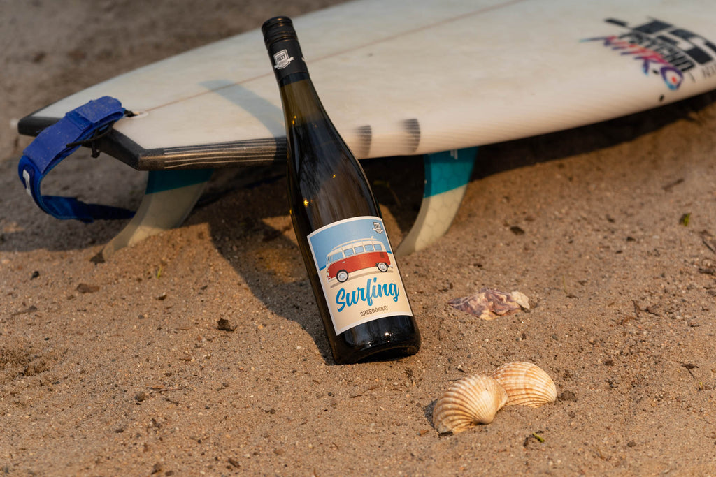 Surfing VW Bulli Chardonnay von Berdoldt Reiff und Nett - Weinflasche an Surfbrett im Sand am Strand